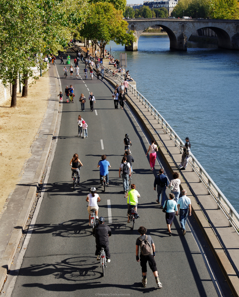 Auf einer breiten Straße entlang des Flusses Seine in Paris laufen Menschen, fahren Fahrrad oder INline-Skates